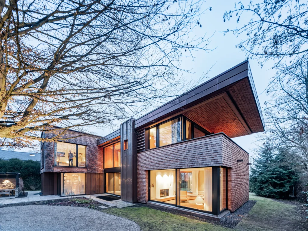 modernes wohnhaus mit holzfassade aus handgefertigten holzschindlen und lichtinszenierung bei dämmerung